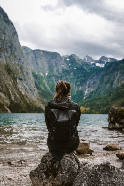 白天，穿着黑色皮夹克的女人站在靠近水体的岩石上